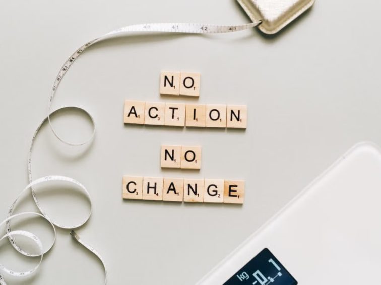 Motivational concept with scrabble tiles spelling no action no change alongside a measuring tape and scale.