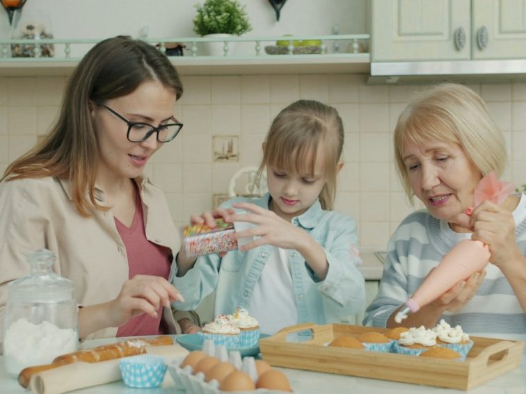 Happy family kid, young mom and senior granny are decorating cupcakes busy with culinary activity in kitchen. Apartment, people and cookery concept.